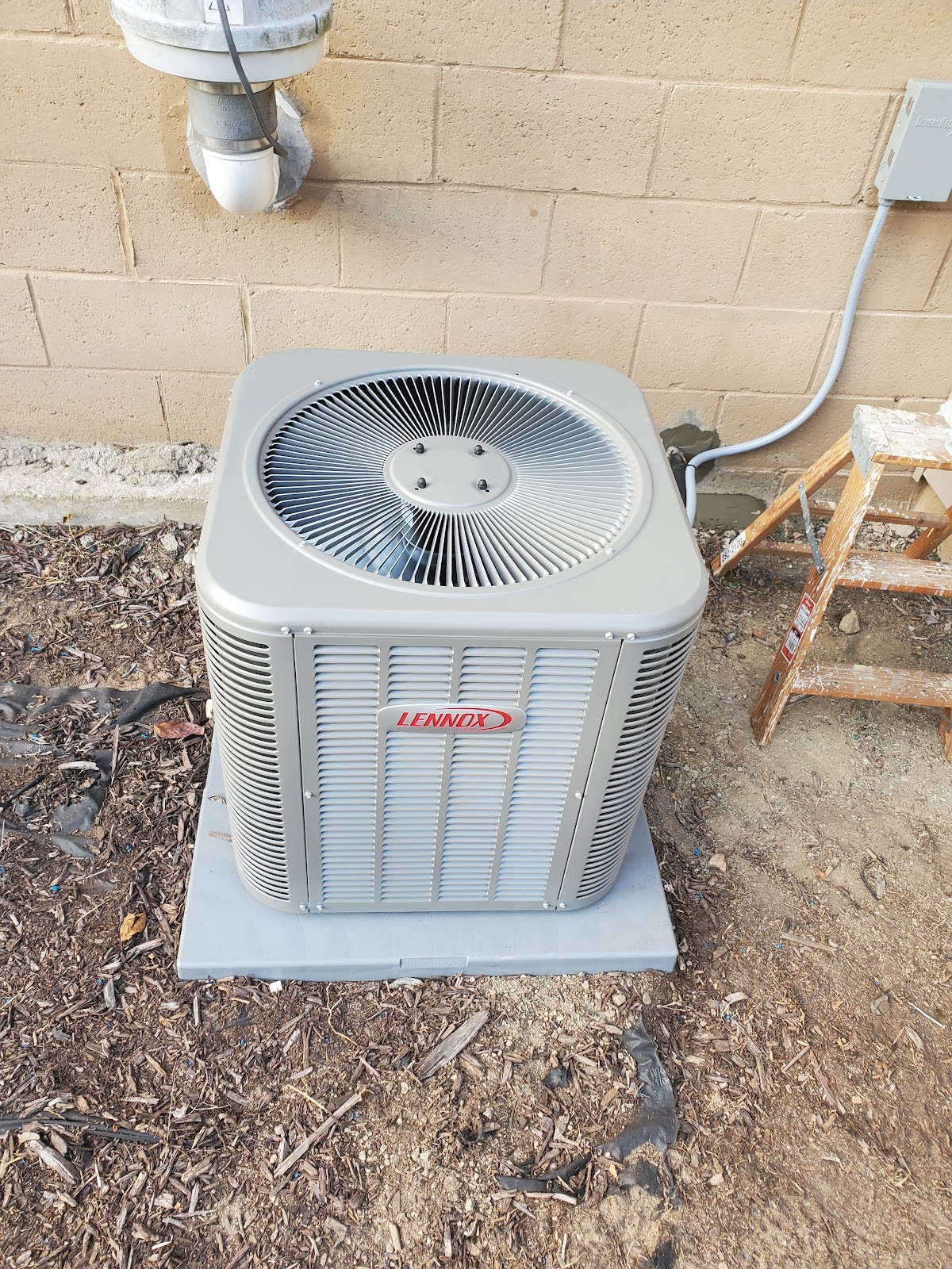 Newly installed Lennox central air conditioning condenser unit on a fresh pad against a house exterior
